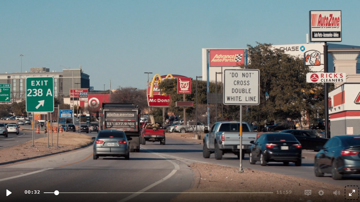 Daytime: Exit 238A highway sign above a strip mall, Chase Bank and other signage on the skyline, traffic on the road.
